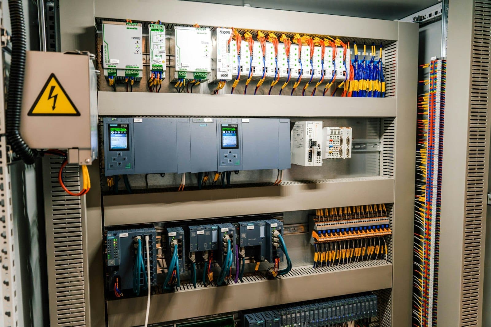 An industrial control cabinet housing PLC modules and rows of wired terminal blocks