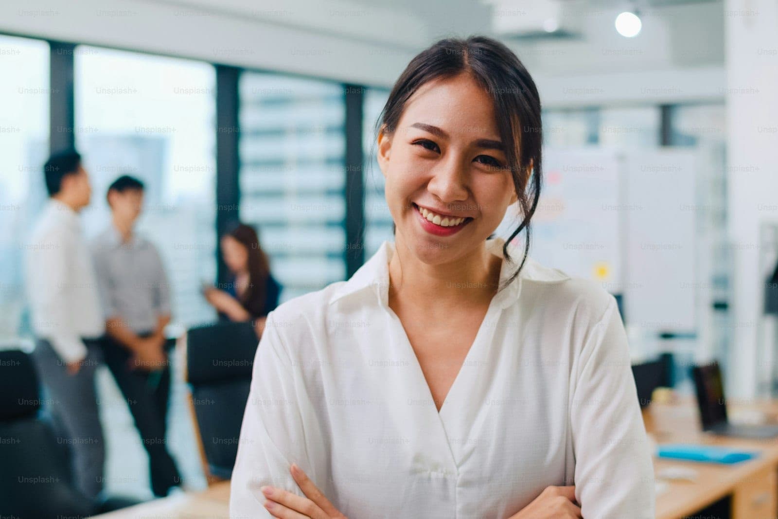 A woman standing confidently in an open-plan office with colleagues working behind her
