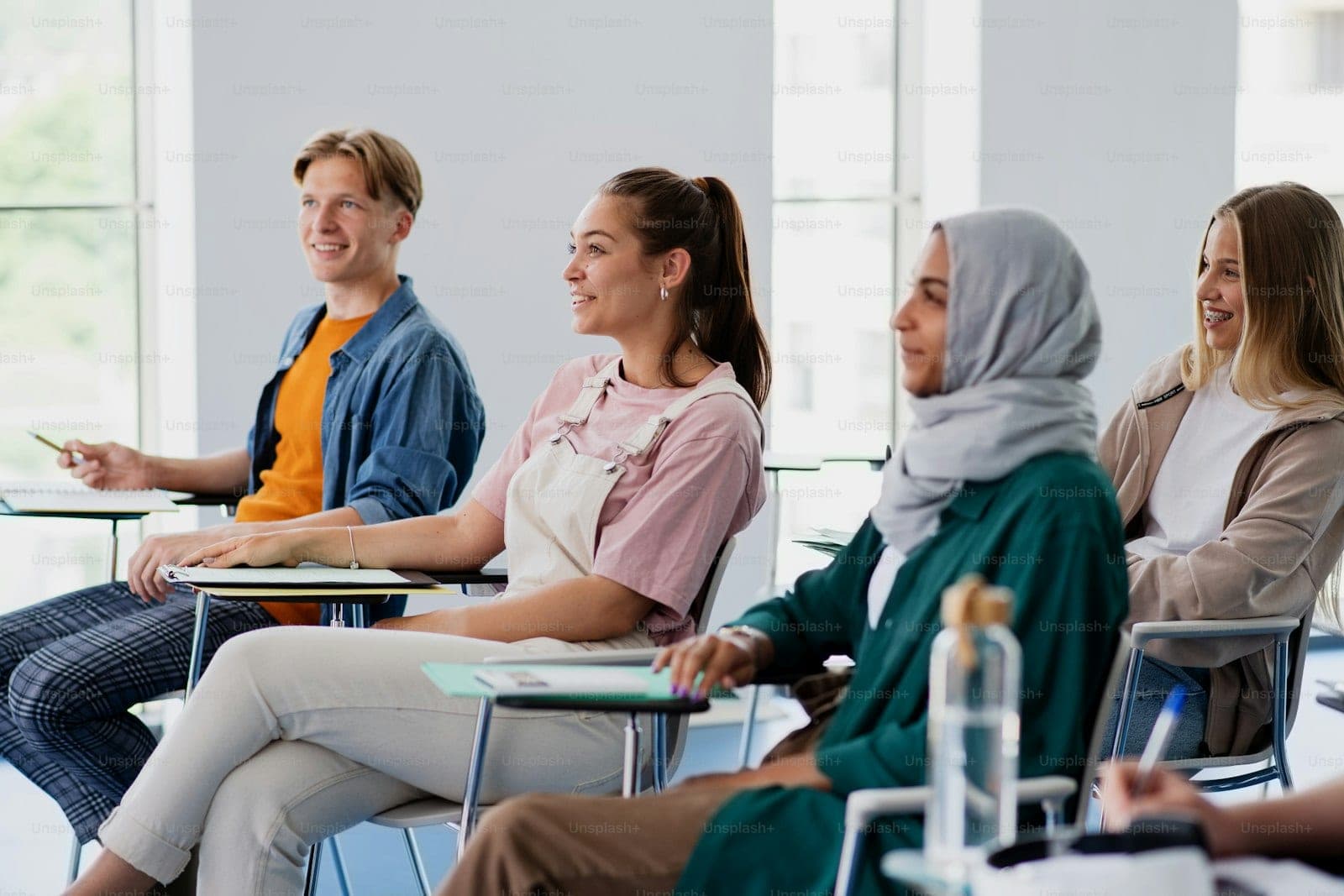 Students seated in a classroom listening, one of them raising a hand