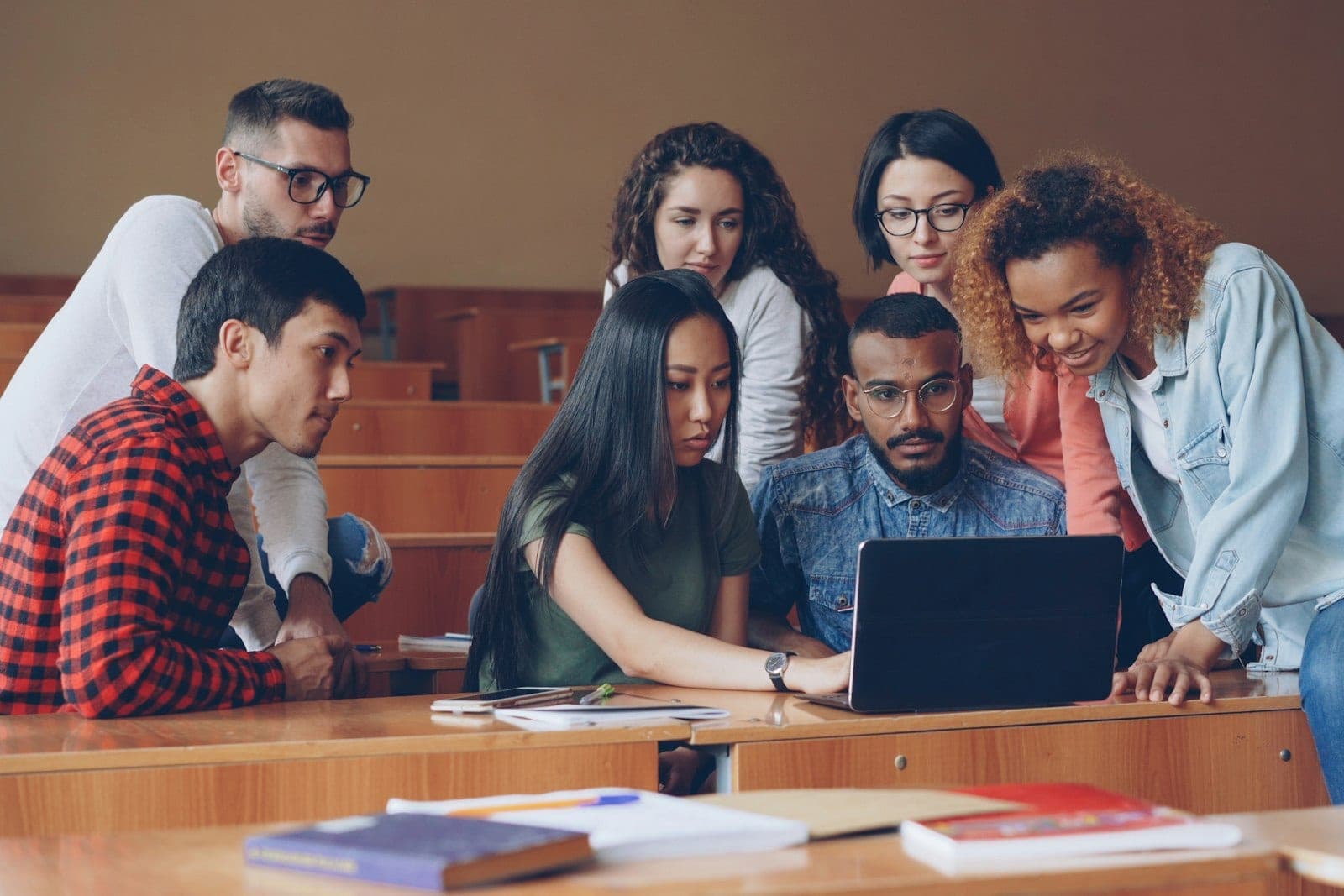A group of students gathered around a single laptop in a lecture theatre, working through something together