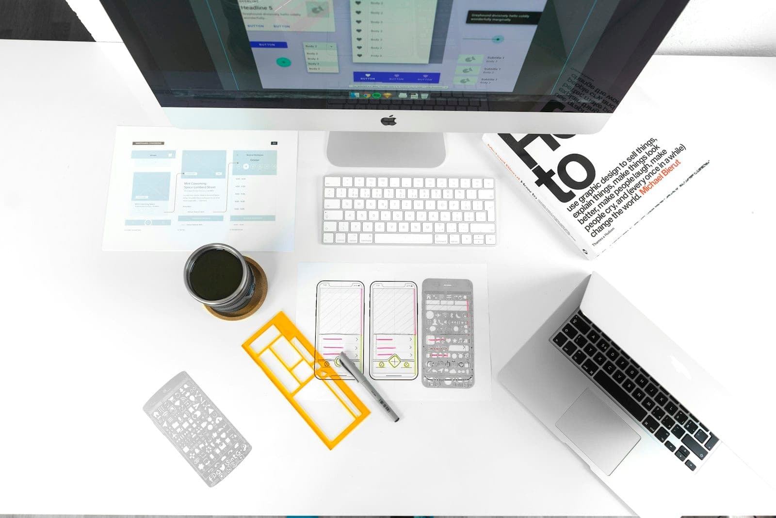 A designer's workstation with interface wireframes laid out beside a monitor