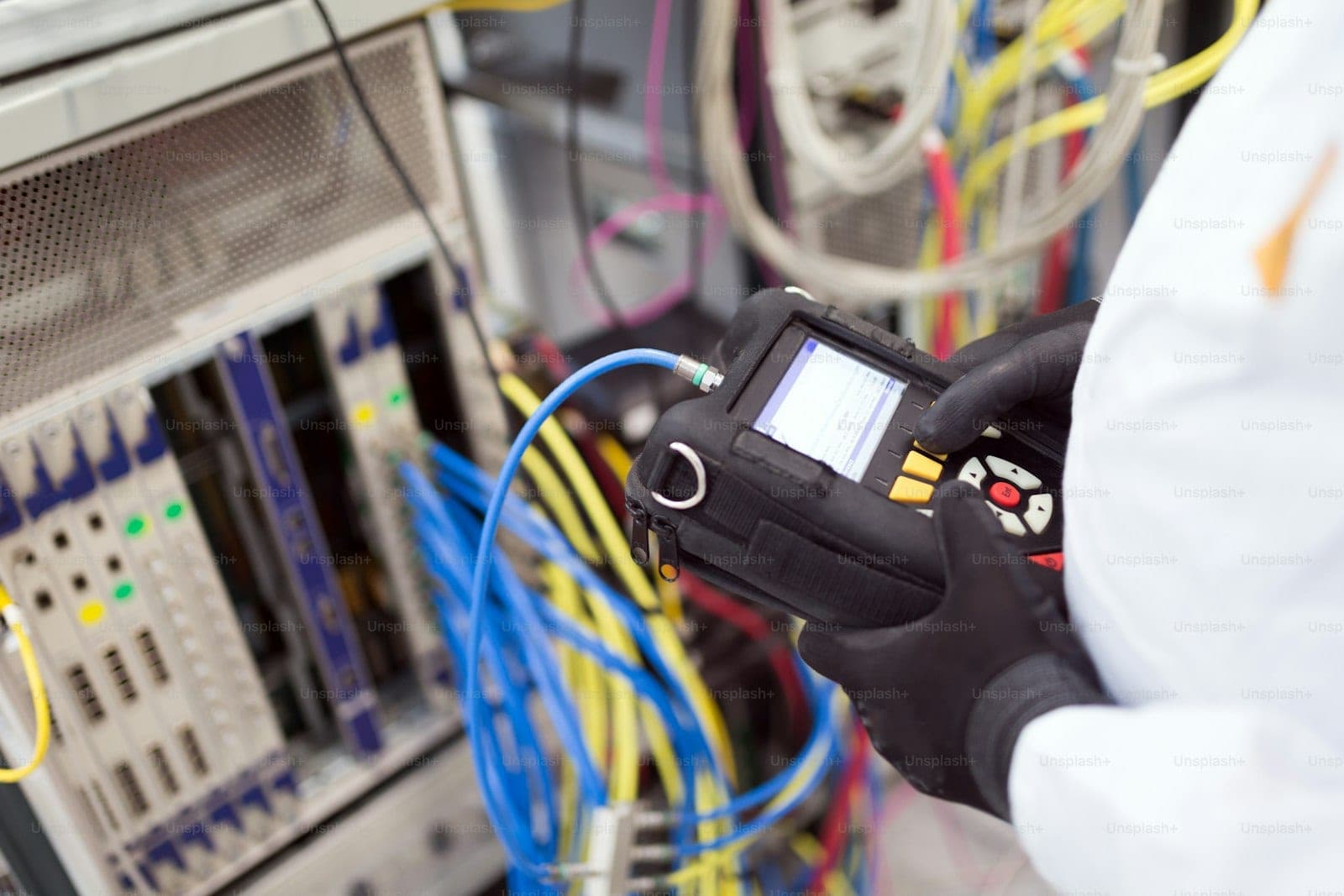 A gloved technician holding a test meter against a patch panel of fibre and copper cabling