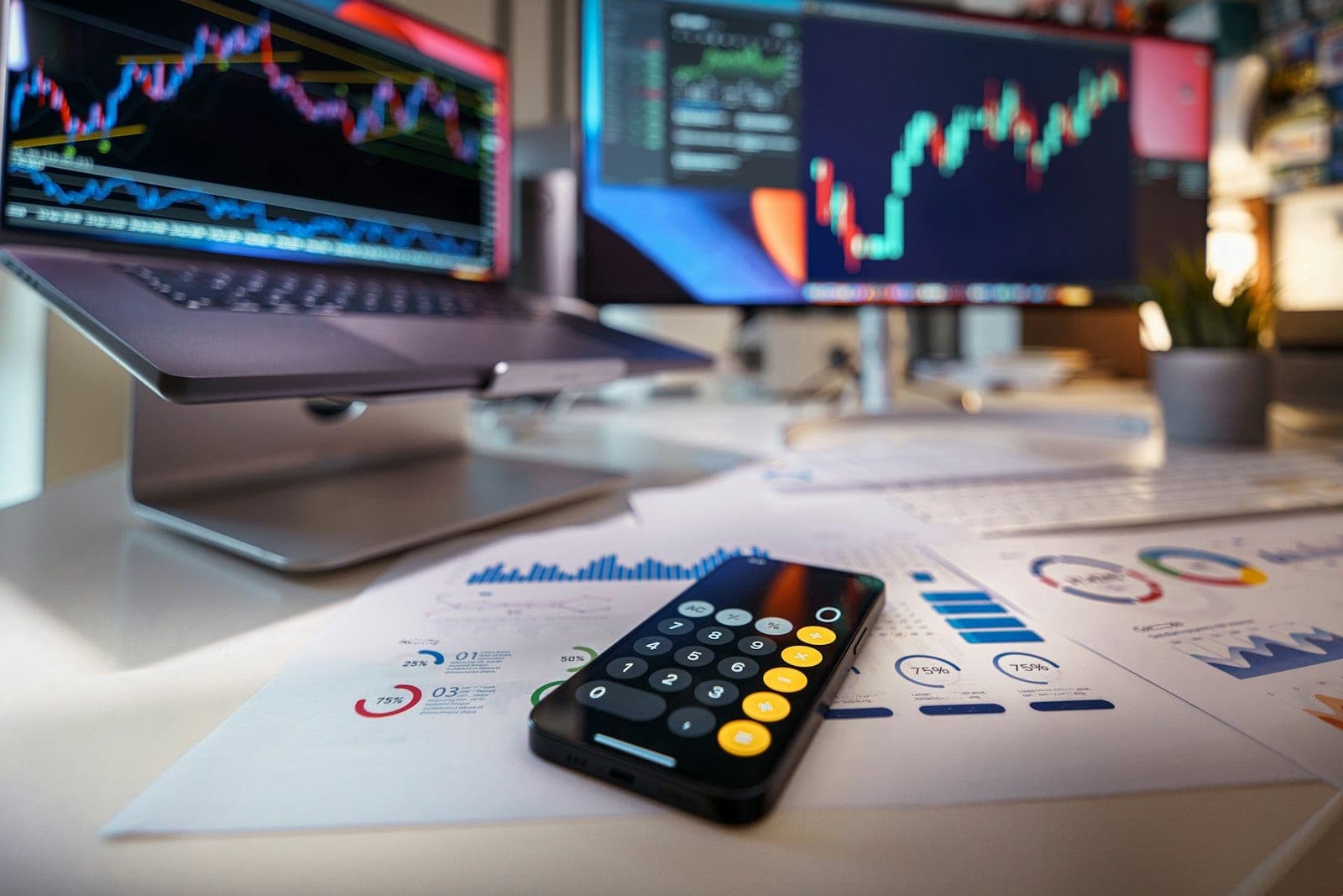 A laptop, printed financial reports and a calculator laid out on a desk