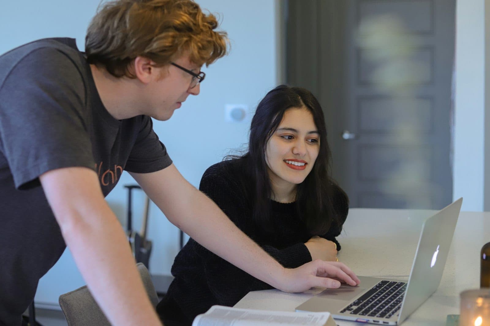 One person leaning over another's laptop, talking them through what is on the screen